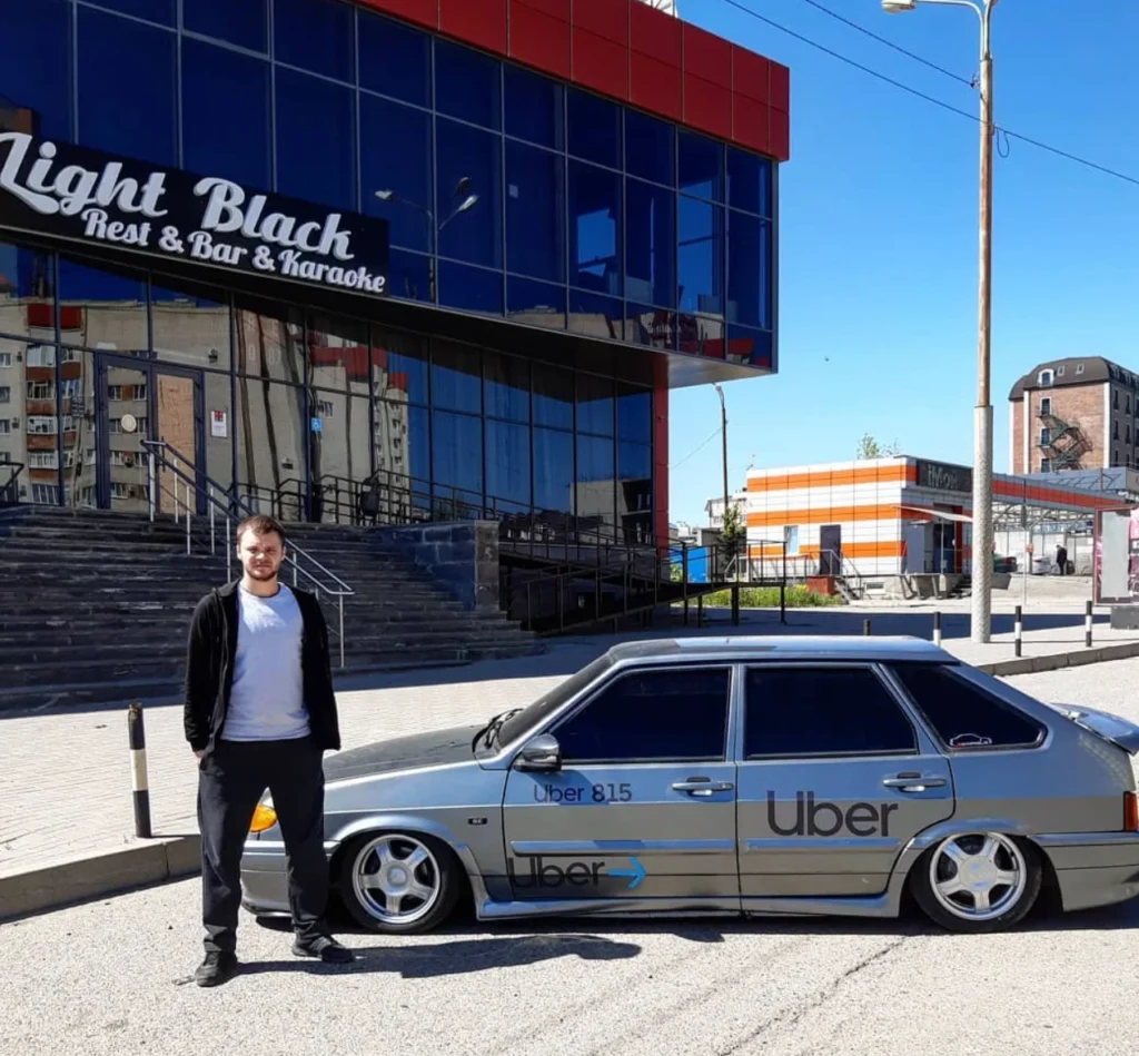 Юра Волков у заниженной серебристой ВАЗ-2114 с наклейками Uber